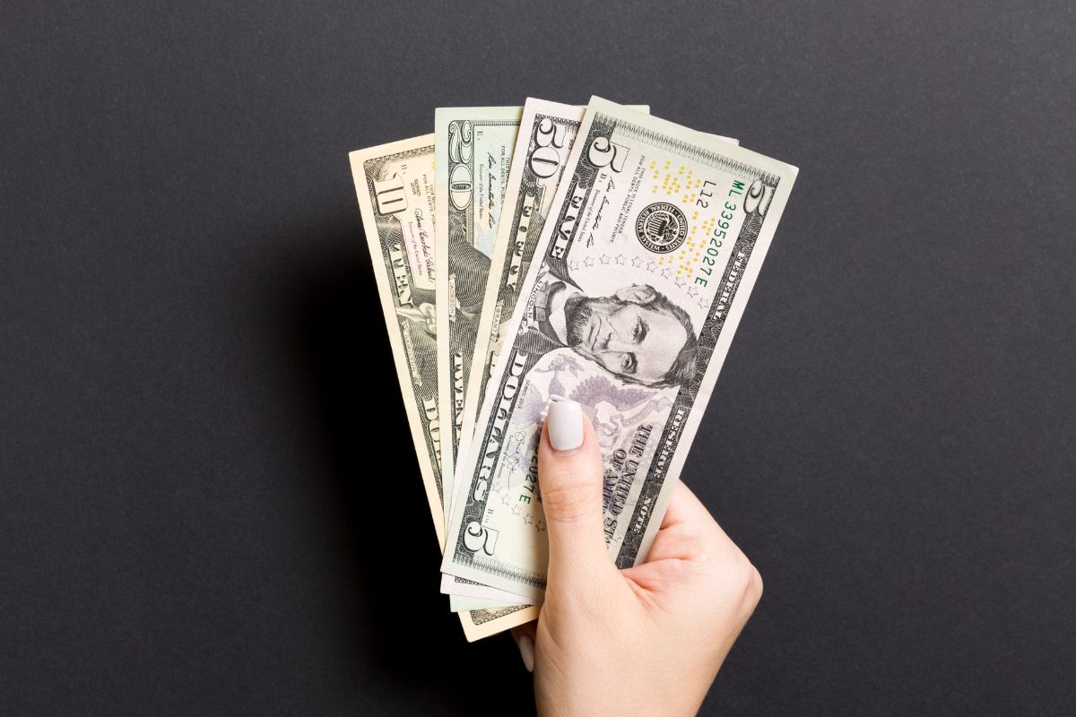 A imagem mostra a mão de uma mulher segurando dinheiro.