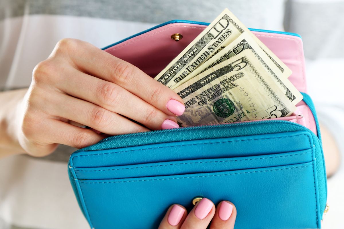 Image of a woman's hand putting her money in her wallet.