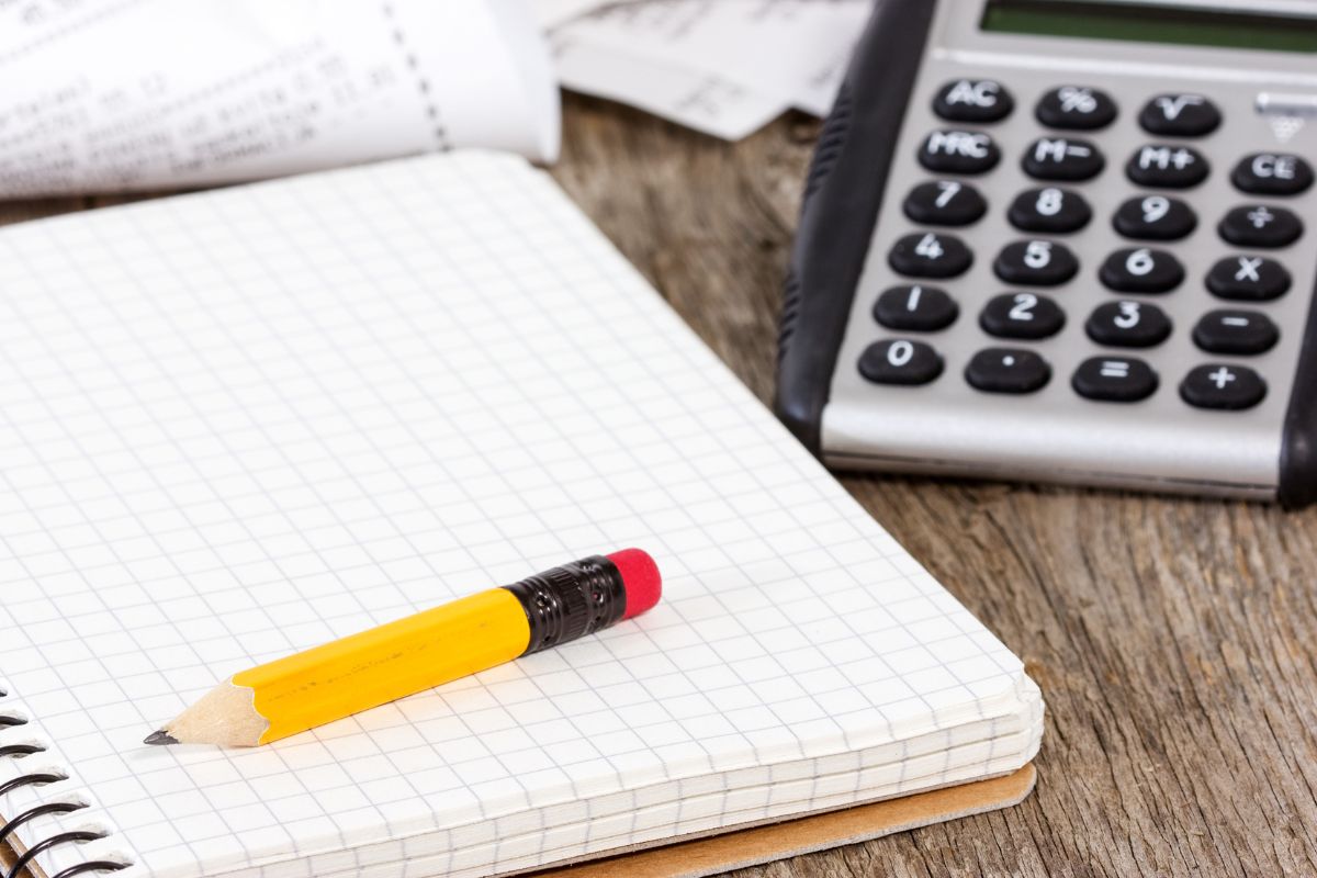 The picture shows a calculator, a pen, and a notebook.