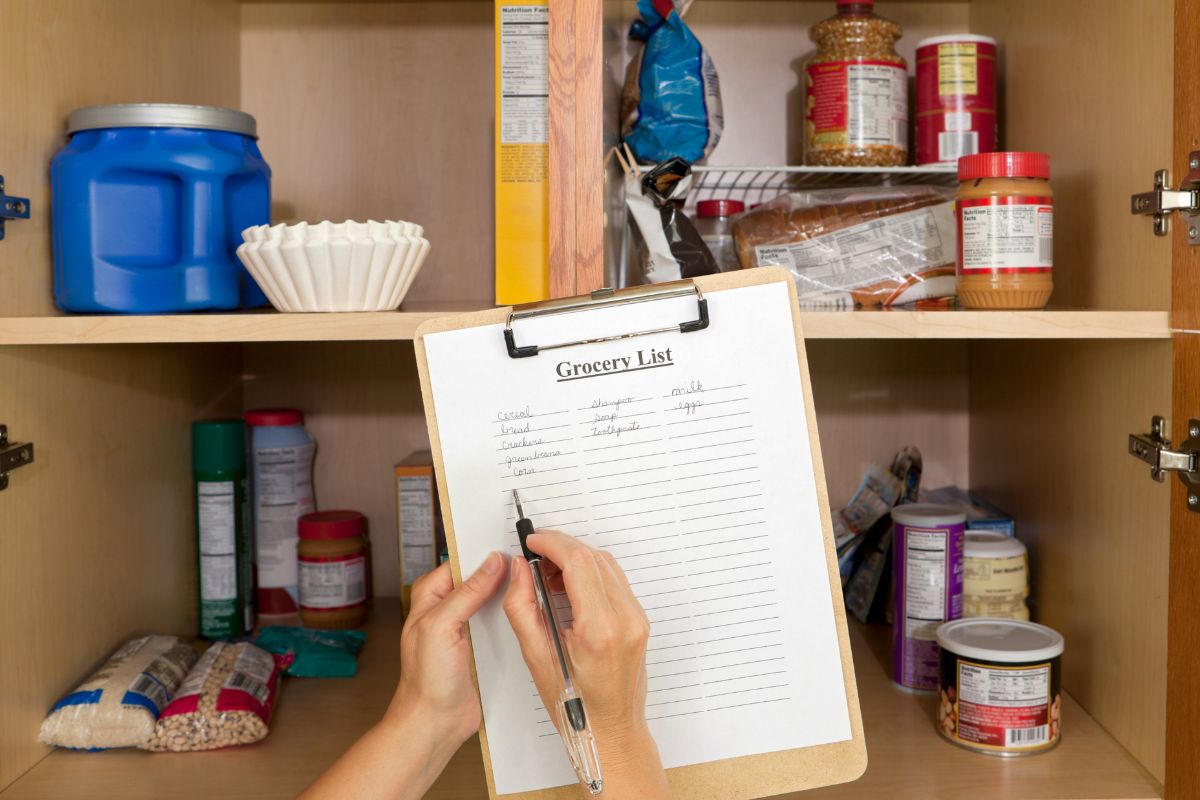 Foto da mão de uma mulher fazendo um inventário em sua despensa.