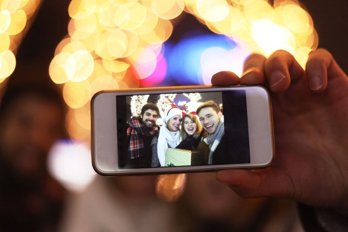The picture shows a group of people taking a picture using a smartphone indicating that giving experience over gifts is often more cost-effective in the long run and is a better value over time.