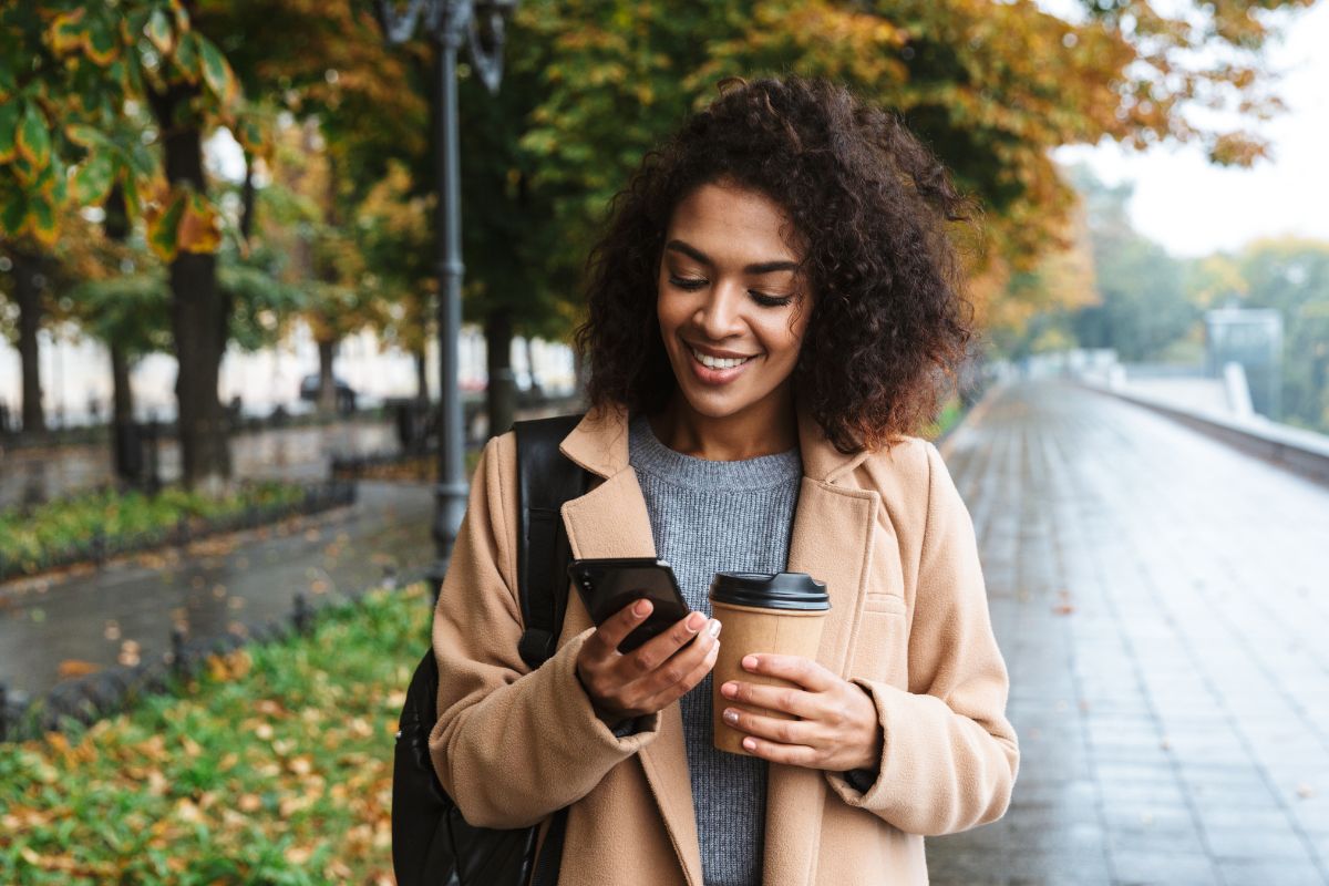 Photo of a woman using a phone while having a coffee.