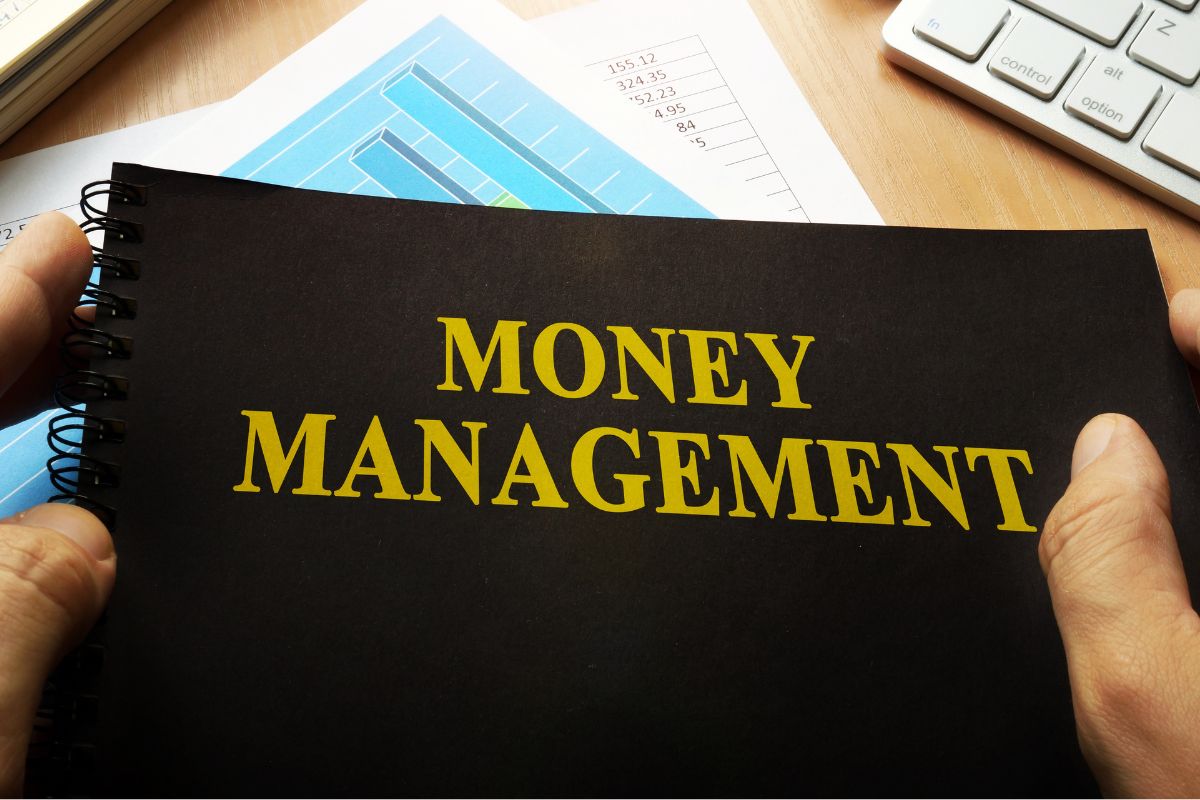 A man's hand holding a notebook with a money management title.