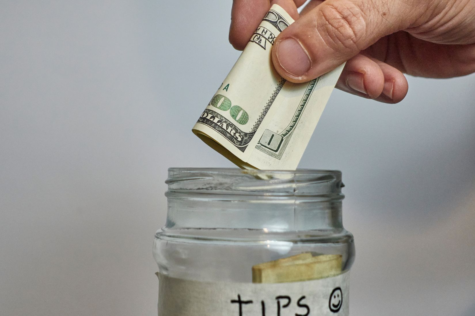 A man's hand putting money in tips jar.