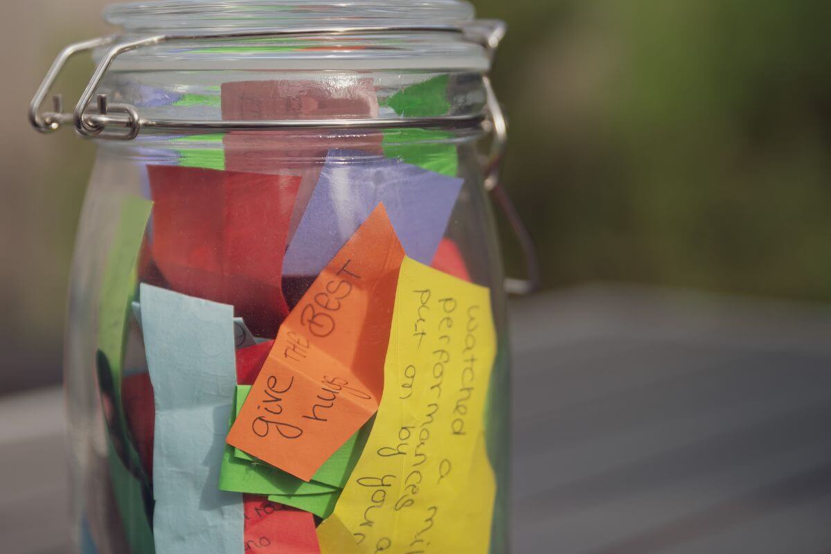 The image shows a jar filled with notes on colored paper indicating to create a gratitude jar where everyone adds short notes of thanks throughout the day.