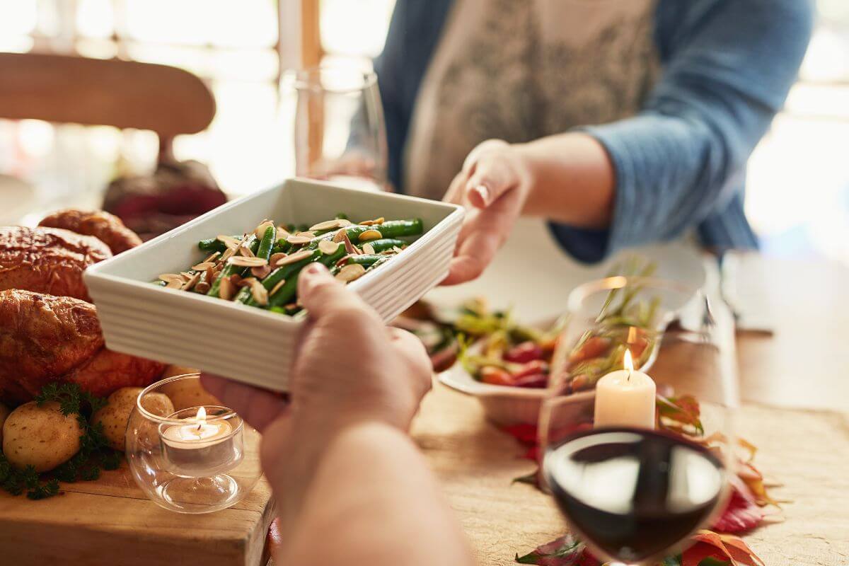 The picture shows food at the table and a girl's hand handing the food to others which refers to sharing a meal with someone on Thanksgiving as a warm way to connect and show gratitude.