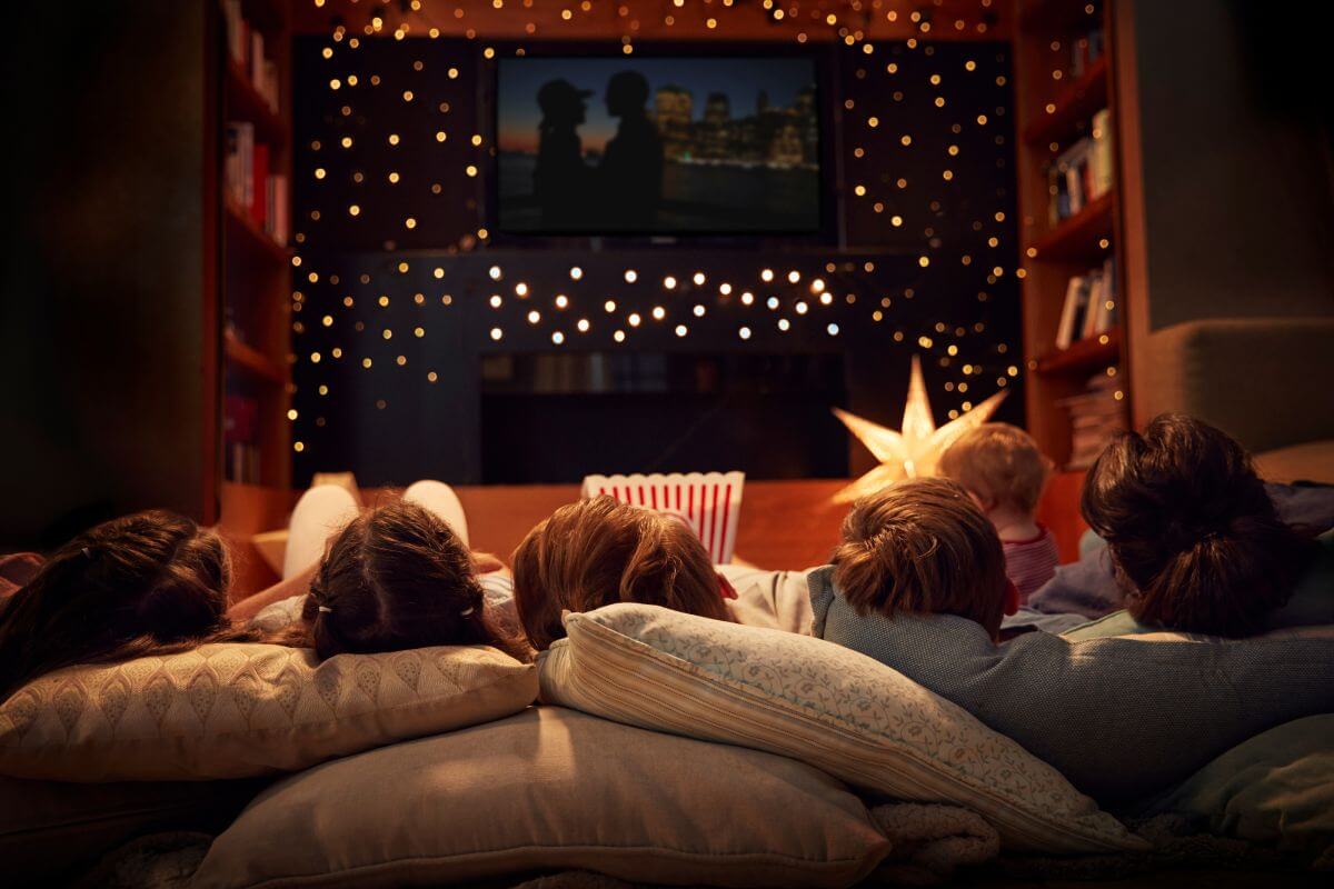 The picture shows Christmas lights and a group of a family with their popcorn enjoying a cozy movie night which is a budget-friendly gift that makes a fun evening for friends or family.