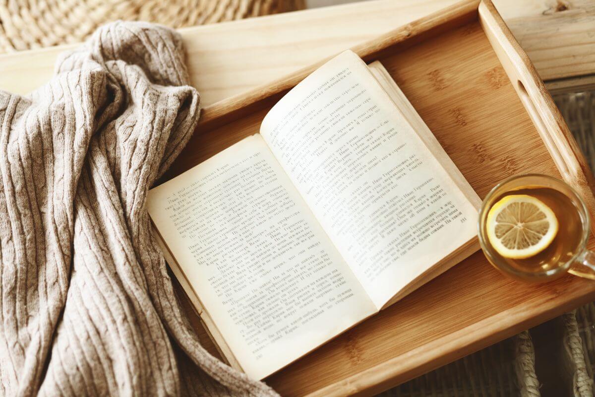 The image show a sweater, a tea with lemon, and a book on the tray which means to gift a book you've enjoy with a personal note that making it deal for book-loving family or friends members.