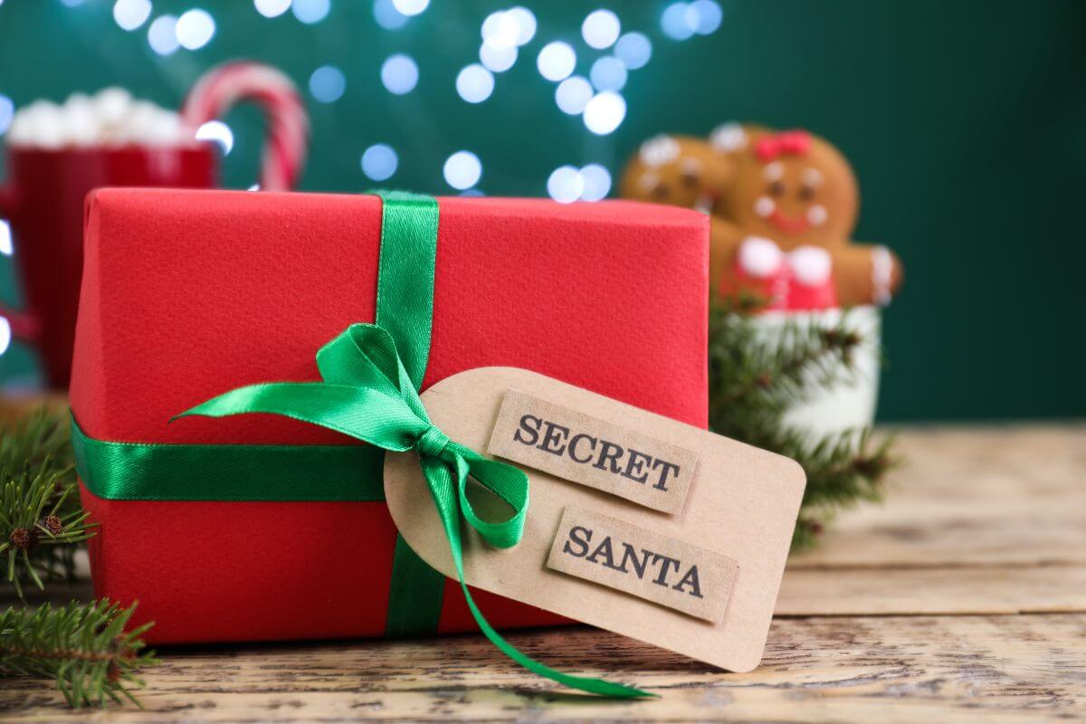 The image of a girt with a tag and notes refers to organizing a group Secret Santa to buy fewer people gifts that keep holiday shopping affordable by focusing on one thoughtful gift.