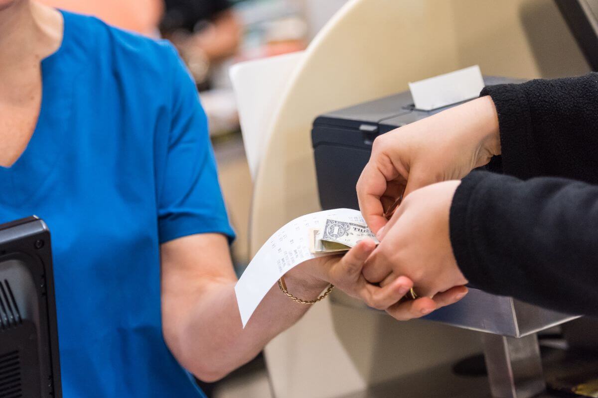 The picture shows a cashier handing the change and a receipt to the customer indicating to use cash for shopping to avoid credit card debt and easier to stick to your budget.