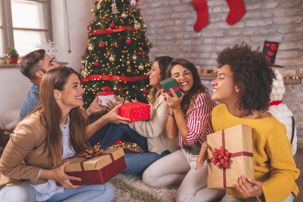 The picture of a Christmas tree and a group of people holding their gifts which means to plan a gift exchange with family is a great way to still give without the stress of multiple gifts.