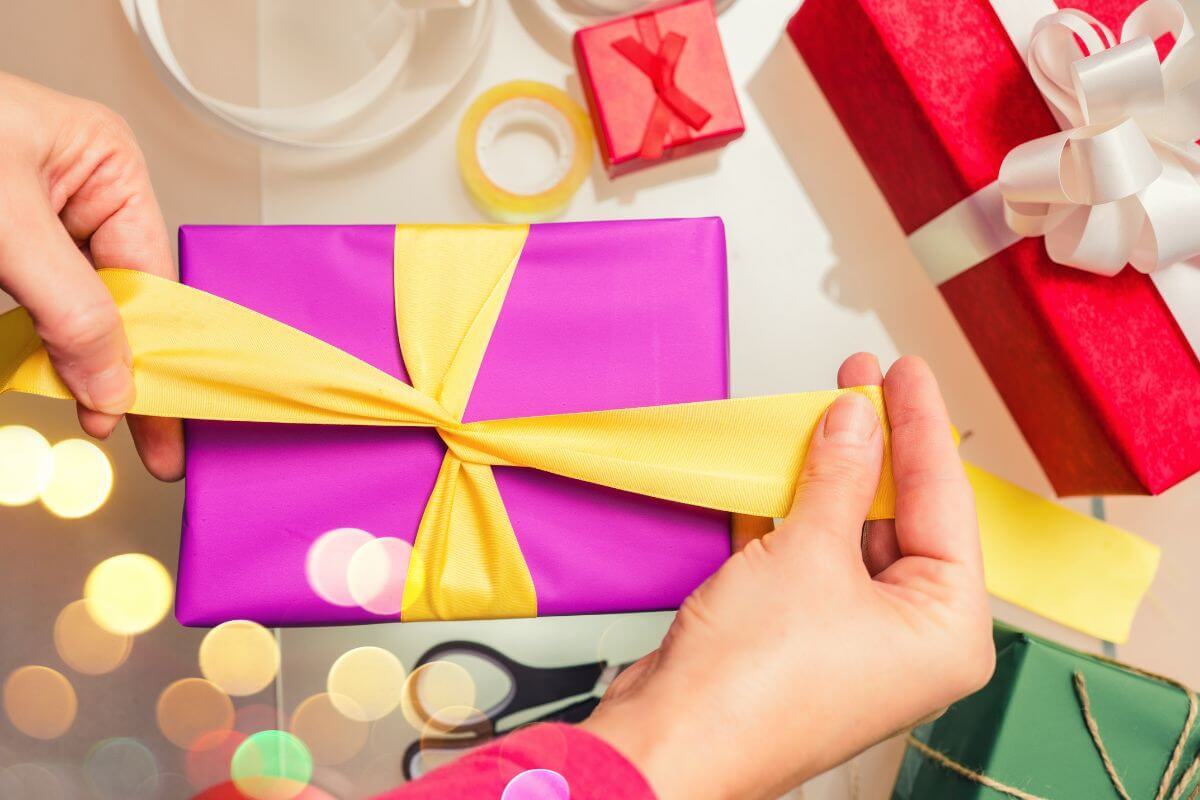 The picture shows gifts and a girl's hand finishing the wrapping of gift indicating to re-gift unused items in great condition without the added cost.