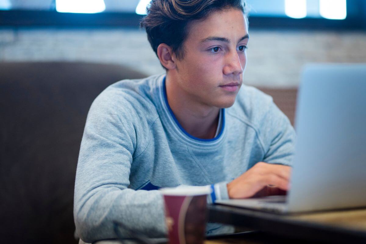 The image shows a teenage boy using a laptop to become a virtual assistant for small business owners and earn extra income while building organizational and communication skills.