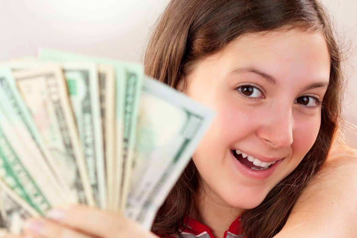 The photo shows a teenage girl holding dollar bills which means exploring these ways to make money as a teen while building a strong foundation for financial independence.