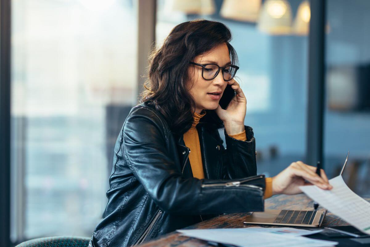The photo tells about a girl looking at the papers while having a call and using a laptop which means to prioritize tasks to maximize productivity and reduces work spillover into personal time.