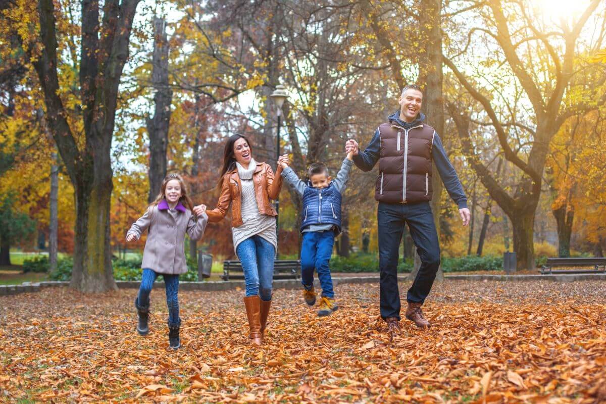 The photo of a happy family walking at the park together means using family downtime for relaxation to reduce stress helps you recharge and strengthens family bonds.