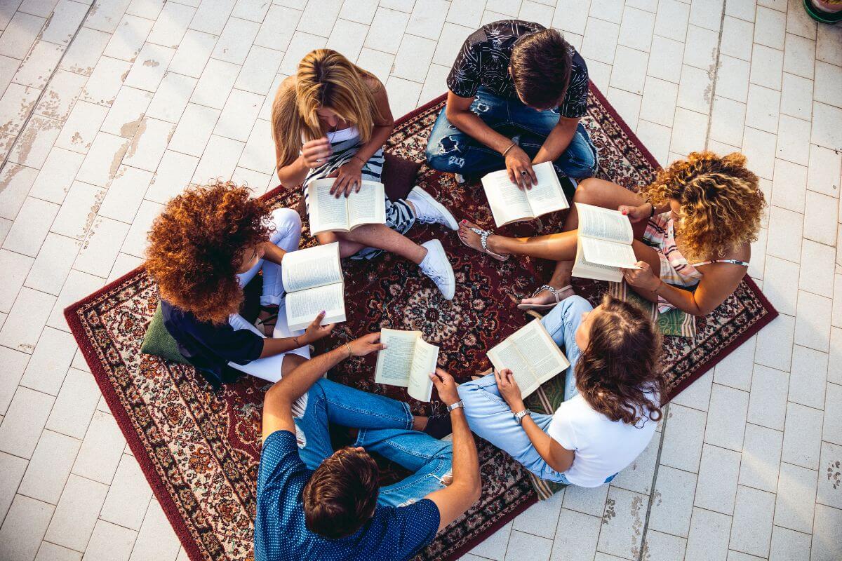The image tells about a group of friends holding a book and having a cozy reading session together and enjoying the calm moments of the day.