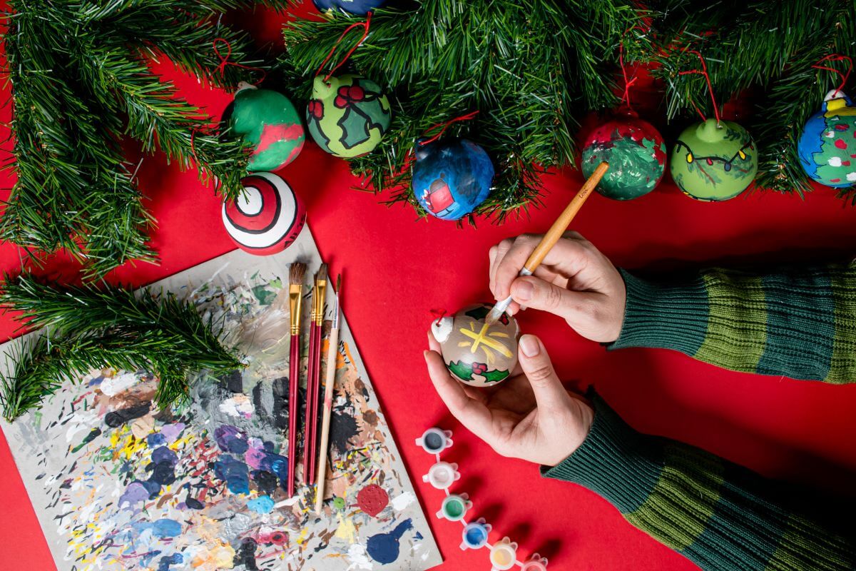 The image of a Christmas tree, painting tools, and a girl's hand painting a ball which means to create homemade ornaments for the tree.