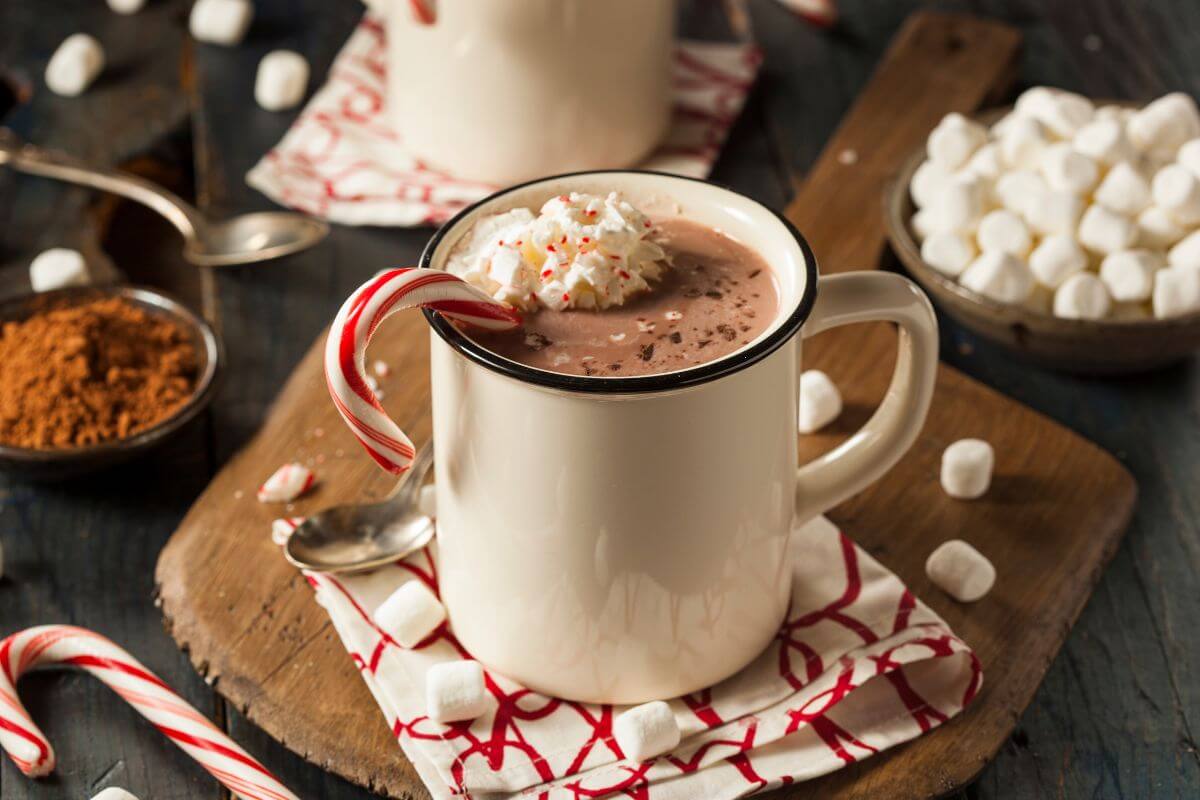The image shows a bowl of marshmallows, coffee, candy canes, and a cup which refers to setting up a hot chocolate bar and letting everyone customize their drink for a cozy and sweet treat.