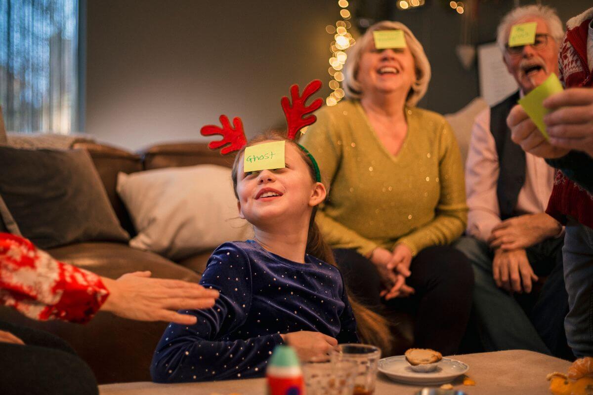 The image shows a group of people with a piece of paper on their forehead indicating that planning a holiday-themed trivia game can be an entertaining way to learn and compete while having fun.