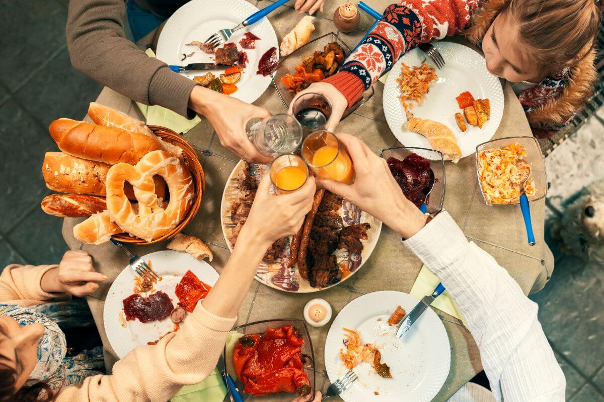 The photo tells about food on the table and a group of family cheers their drinks together which means having a Christmas day picnic indoors to spend time together and make the day feel special.