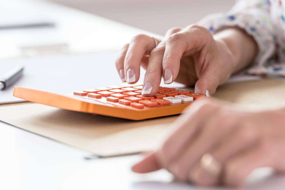 The photo tells about the girl's hand using a calculator indicating that reviewing your spending and creating a budget can prevent overspending and put you on the path to financial stability.