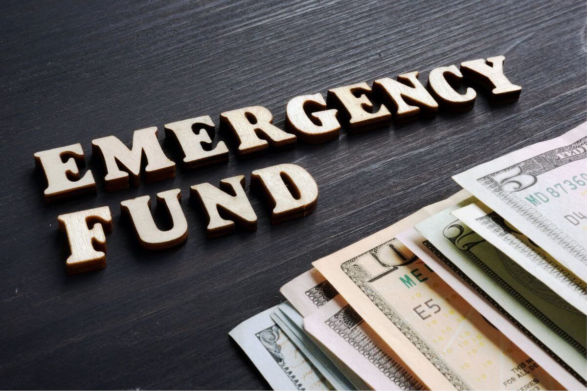 The image shows dollar bills and letters on the table indicating to set up an emergency savings fund for unexpected expenses and a key step toward being financially sound.