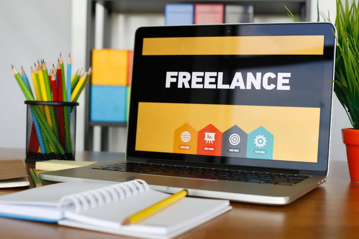 The photo of colored pens, a notebook with a pen, and a laptop with a screen display refers to increasing your income through freelance work as a proactive way to recover financially after overspending.