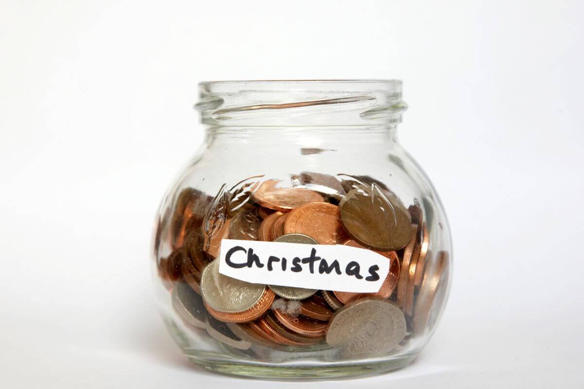 The picture shows a jar filled with coins and notes referring to building up your savings for the next holiday season helps reduce stress and prevent debt.