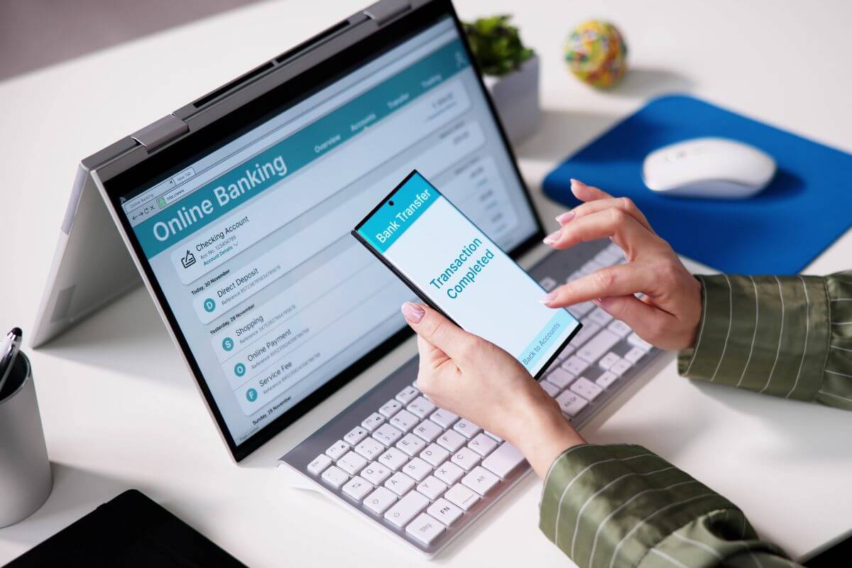 The photo tells about a girl's hand using a laptop and a phone which means automated savings and bill payments that keep you schedule and helps avoid late fees.