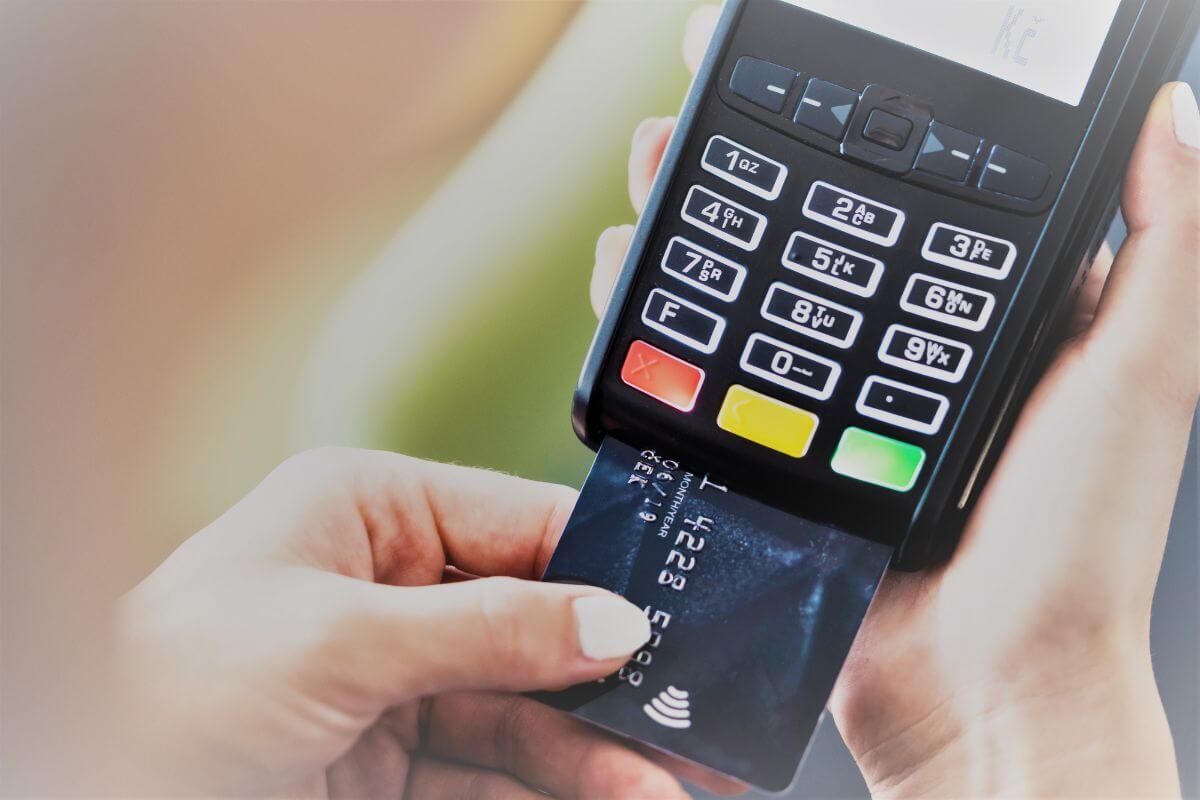 The picture shows a man's hand holding a scanner machine and inserting a card which means credit card debt that exceeds 30% of your limit can hurt your credit score and increase stress.