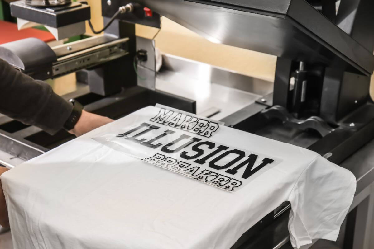 The picture tells about a man's hand designing a shirt by printing in a machine and selling merchandise online to make extra income.