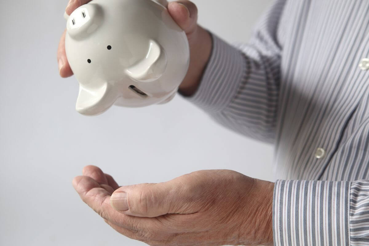 The photo shows an old man's hand withdrawing an empty piggy bank indicating to unable to save due to debt is a sign you have too much debt.