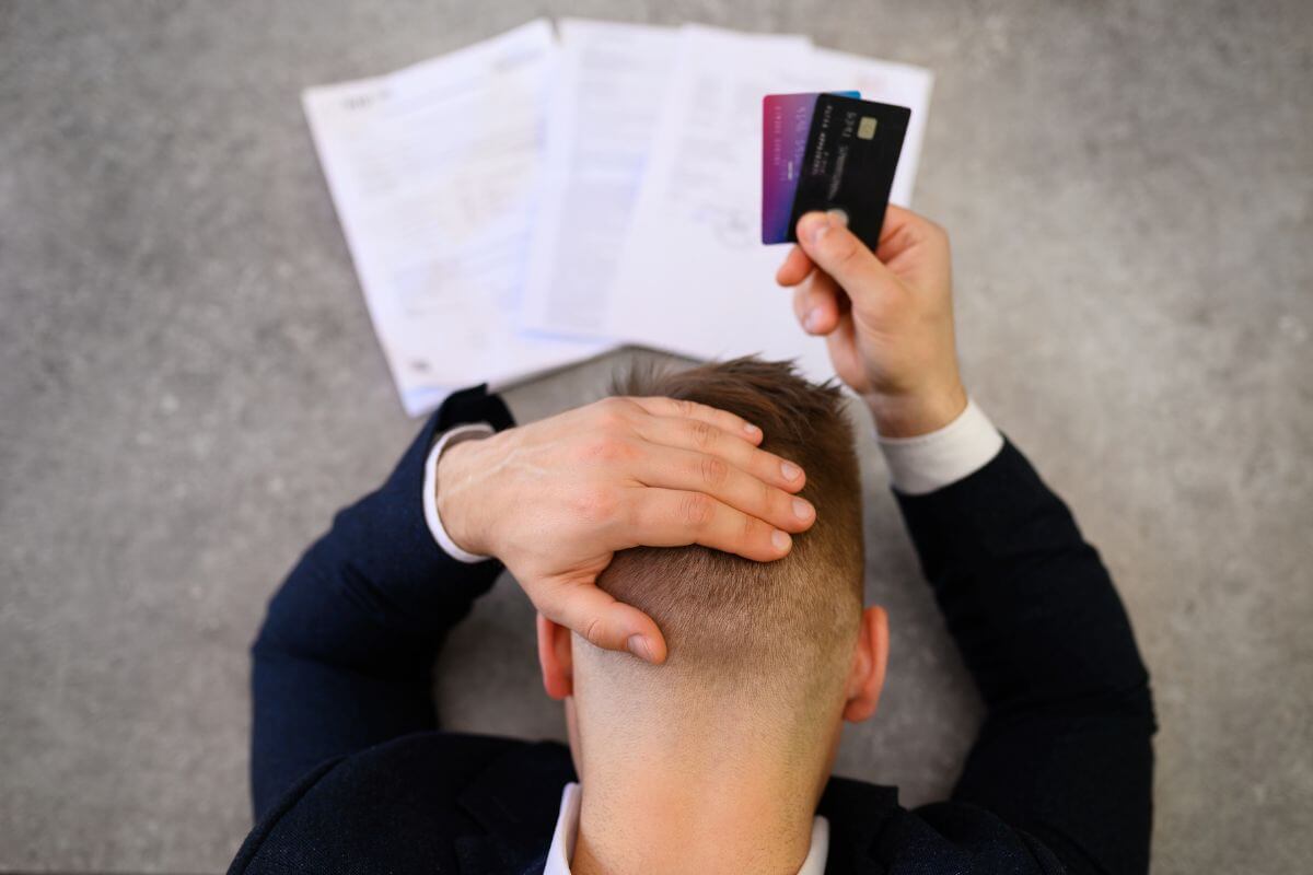 The photo shows papers on the table and a man holding cards while holding his head indicating that reaching or exceeding your limit can lead to too much debt.