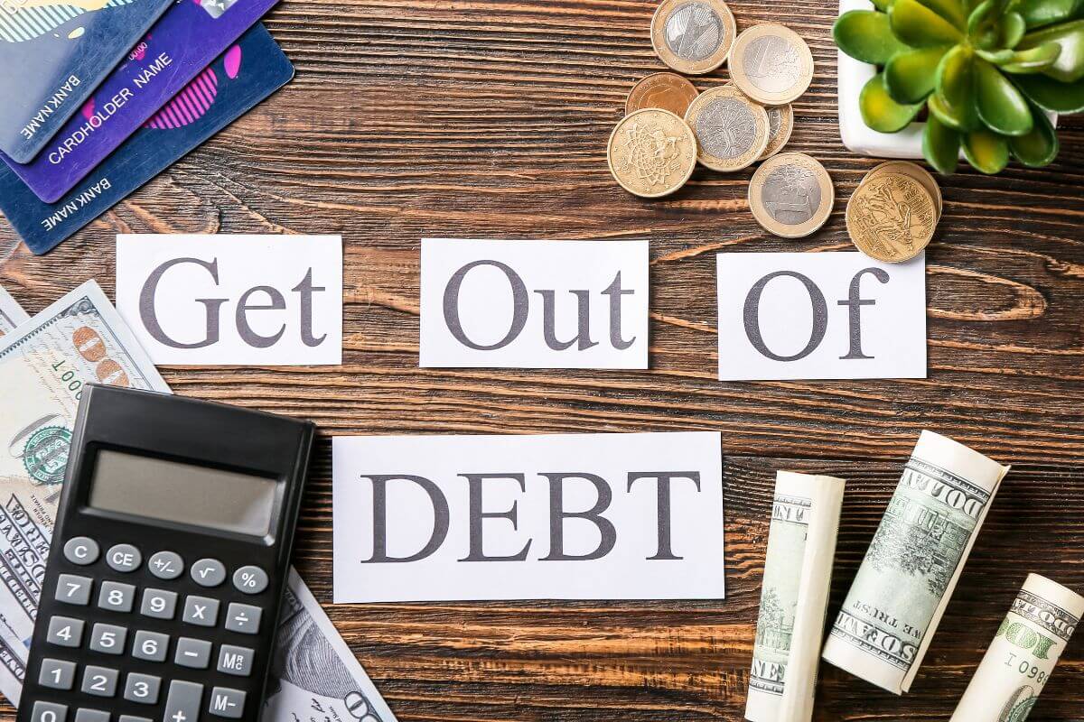 The photo shows a plant, coins, credit cards, dollar bills, a calculator, and papers with notes which means to learn how to get out of debt today and make a plan for long-term financial independence.