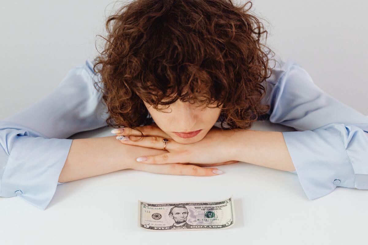 The image tells about a girl bent on the table and looking at a dollar bill which means acknowledging that financial struggles are common and it's important to accept and realize you're not alone.