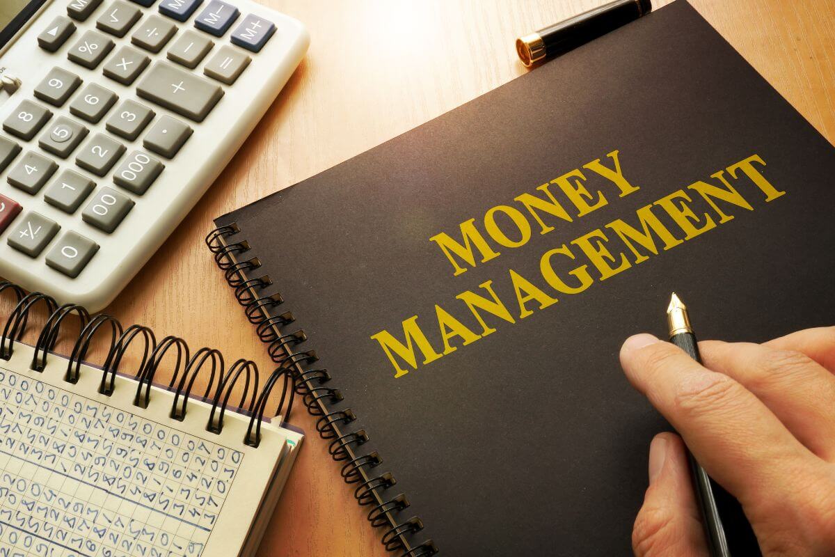 The photo of a calculator, a notebook, and a black-covered book with notes and a man's hand holding a pen indicates that educating yourself on money management can help you build strong financial skills.