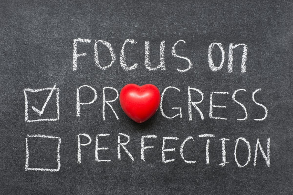 The picture tells about a blackboard with notes, checks, and a red heart which means to focus on progress, not perfection to stay motivated and keep moving in the right direction.
