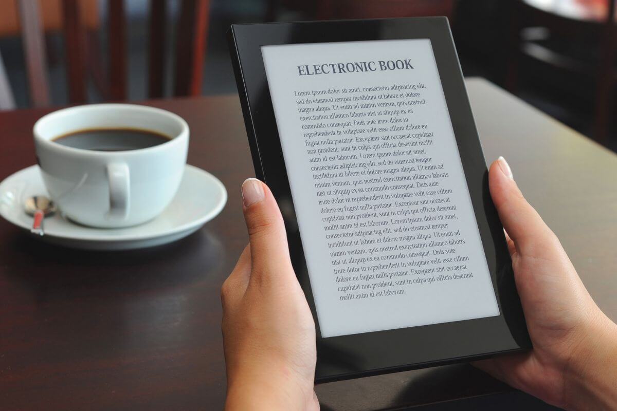 The picture shows a coffee and a girl's hand holding a tablet device which means writing and selling e-books on niche topics is a great way to earn passive income over time.