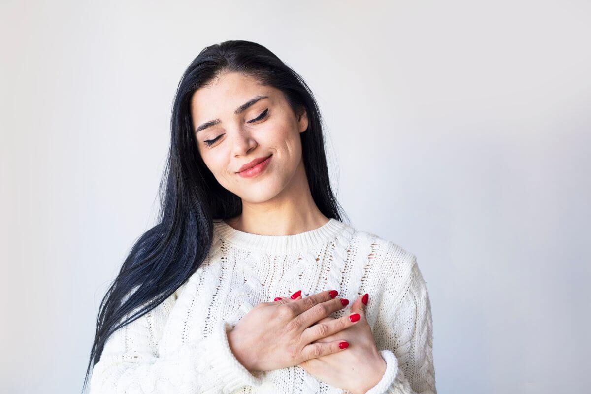 The image tells about the girl putting her hands to her chest which shows practicing self-compassion to be kind to yourself when dealing with financial challenges.