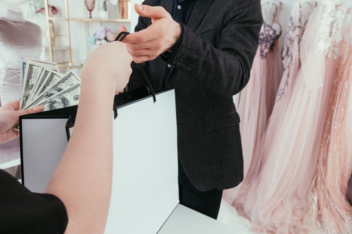 The picture shows dresses and a cashier giving the box to a customer with dollar bills on her hands which means avoiding lifestyle inflation and keeping spending low even in income increases and using extra income to pay down debt and build savings.
