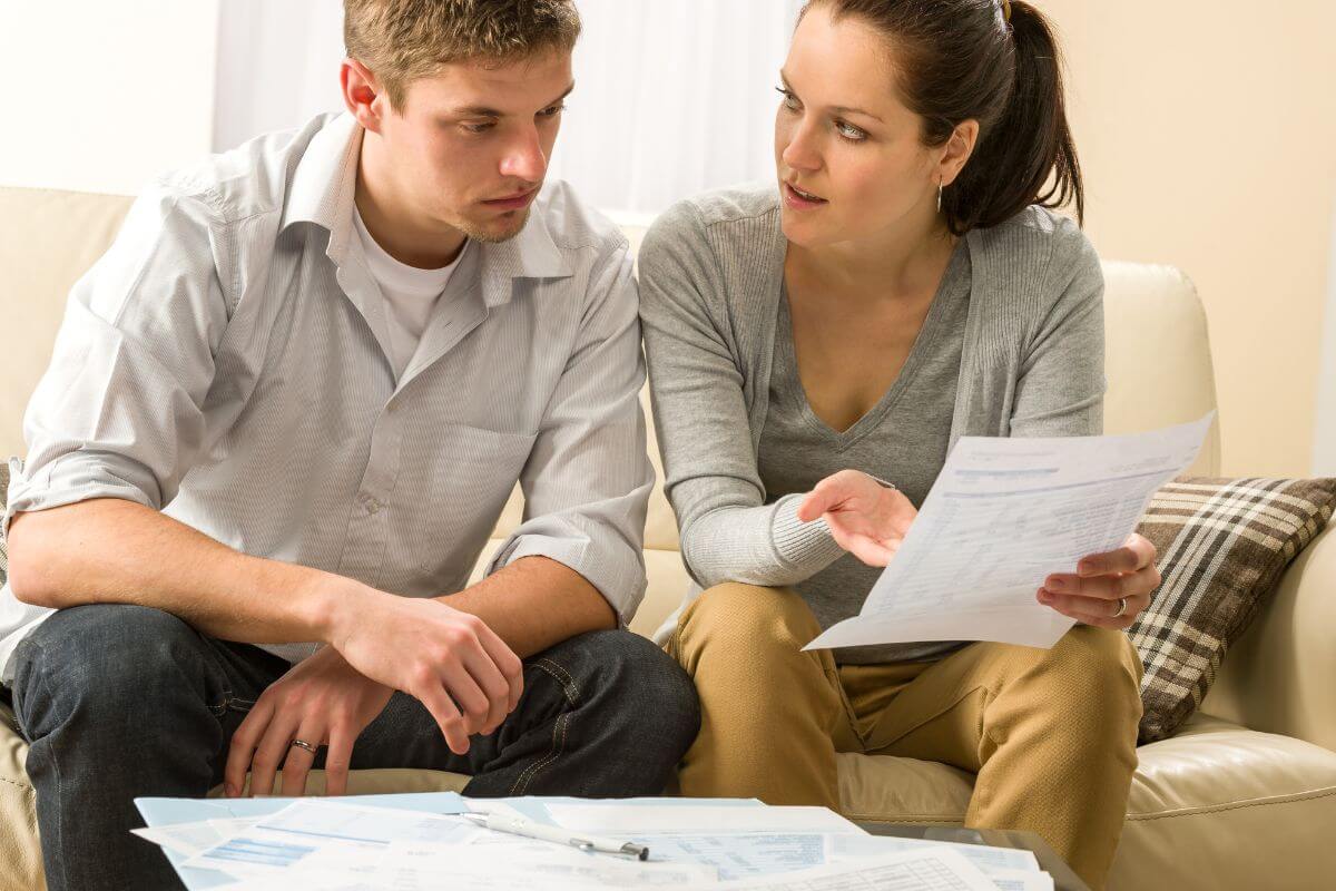 The picture shows a couple talking about the papers on the table which refers to being open and honest about financial goals and concerns that created a safe space for working together on your finances and building trust.