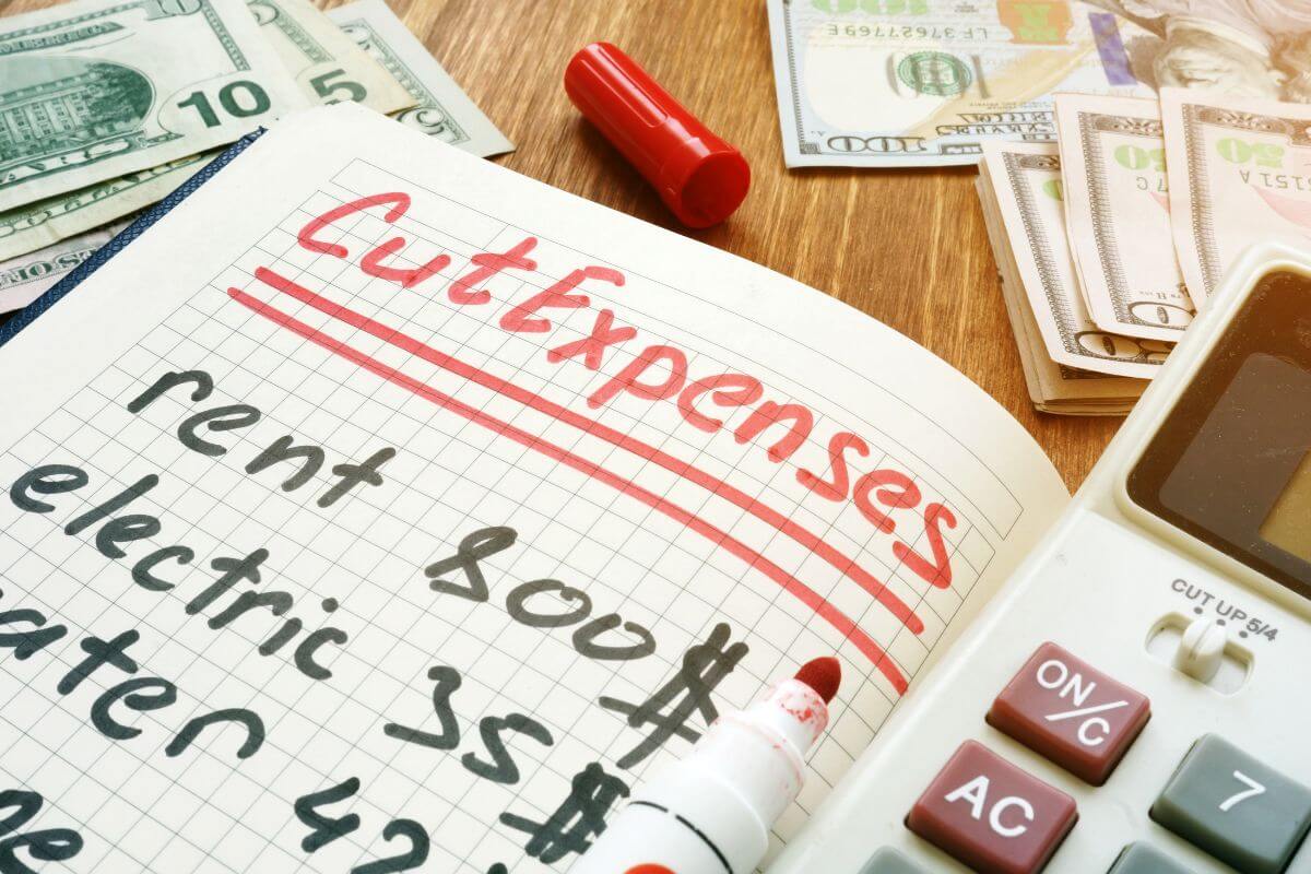 The photo shows dollar bills on the table, a calculator, and a notebook with notes referring to cutting unnecessary expenses and prioritizing debt payments that can redirect that money toward your debts for quicker progress.