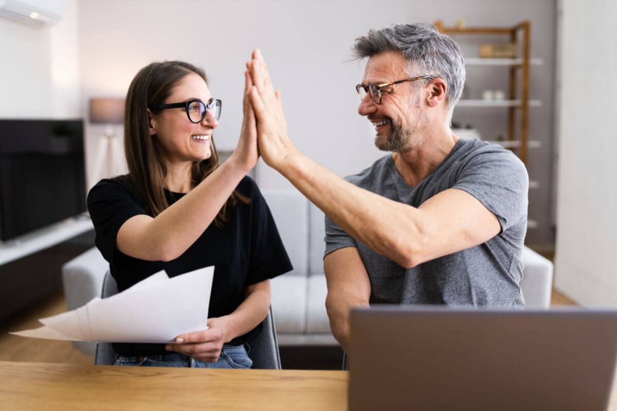 The photo shows a couple holding papers and using a laptop which means sharing financial success, sharing both the good and bad keeps the discussion balanced and positive.