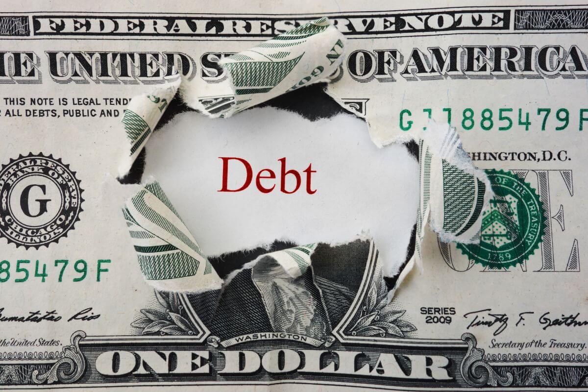 The image shows a dollar bill with a hole and a piece of paper with a note referring to the use of the debt snowball or avalanche method to tackle debt effectively.