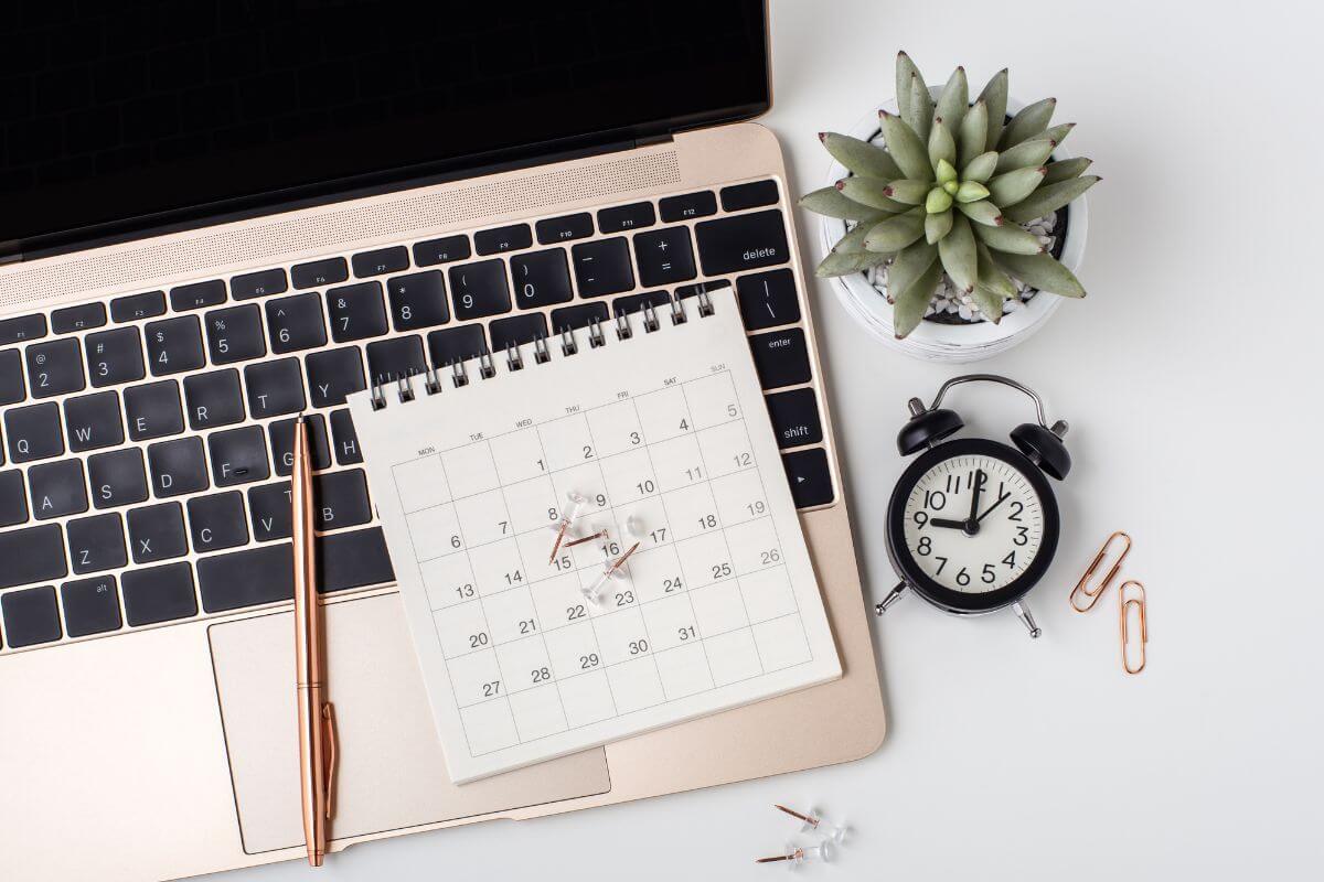 The photo tells about a plant, clock, pins, a laptop, a pen, and a calendar indicating to schedule regular check-ins to address problems early and celebrate progress together.