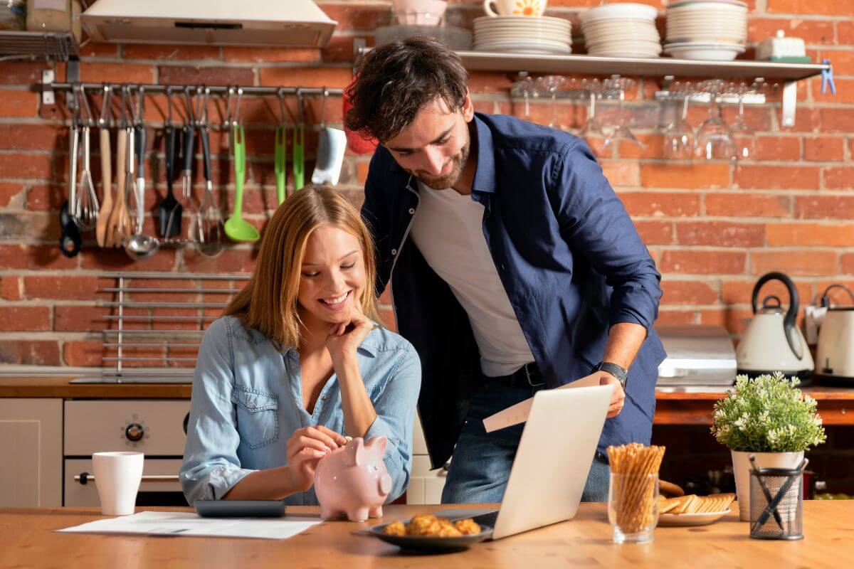 The image of kitchen utensils, papers on the table, a calculator, snacks, a plant, and a couple holding a paper and dropping money in the piggy bank which means focusing on Being independently wealthy and working together and creating a secure future for both of you.