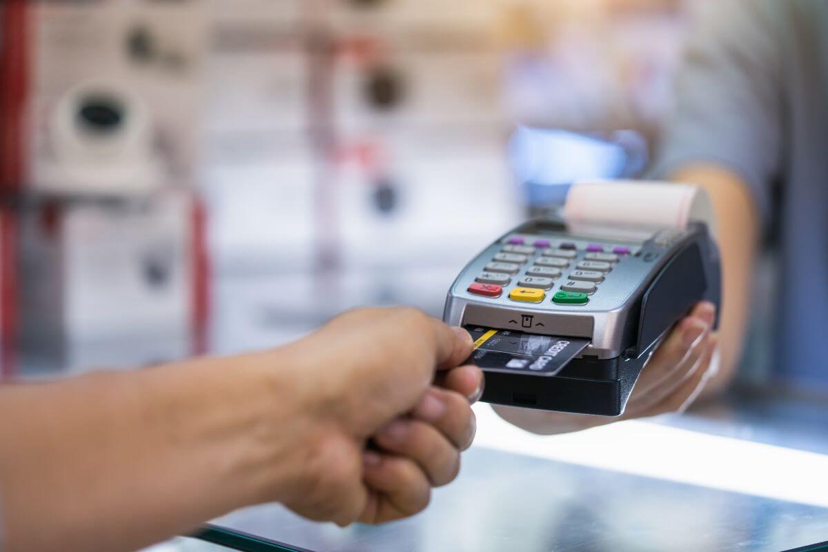 The image shows a cashier holding a card swiping machine and a customer's hand inserting the credit card into it which means to stop using credit cards and focus on reducing what you owe without creating new balances.