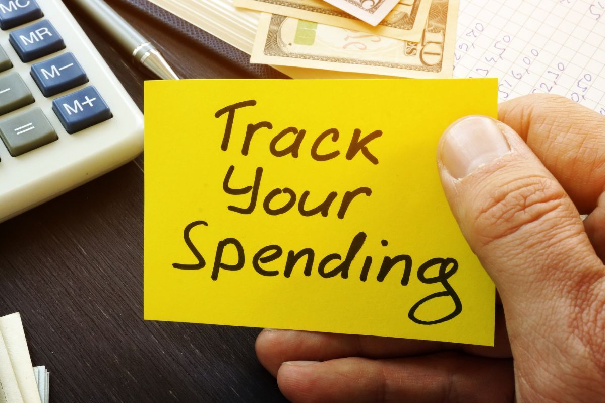 A man's hand holding a paper with Track your Spending wording.
