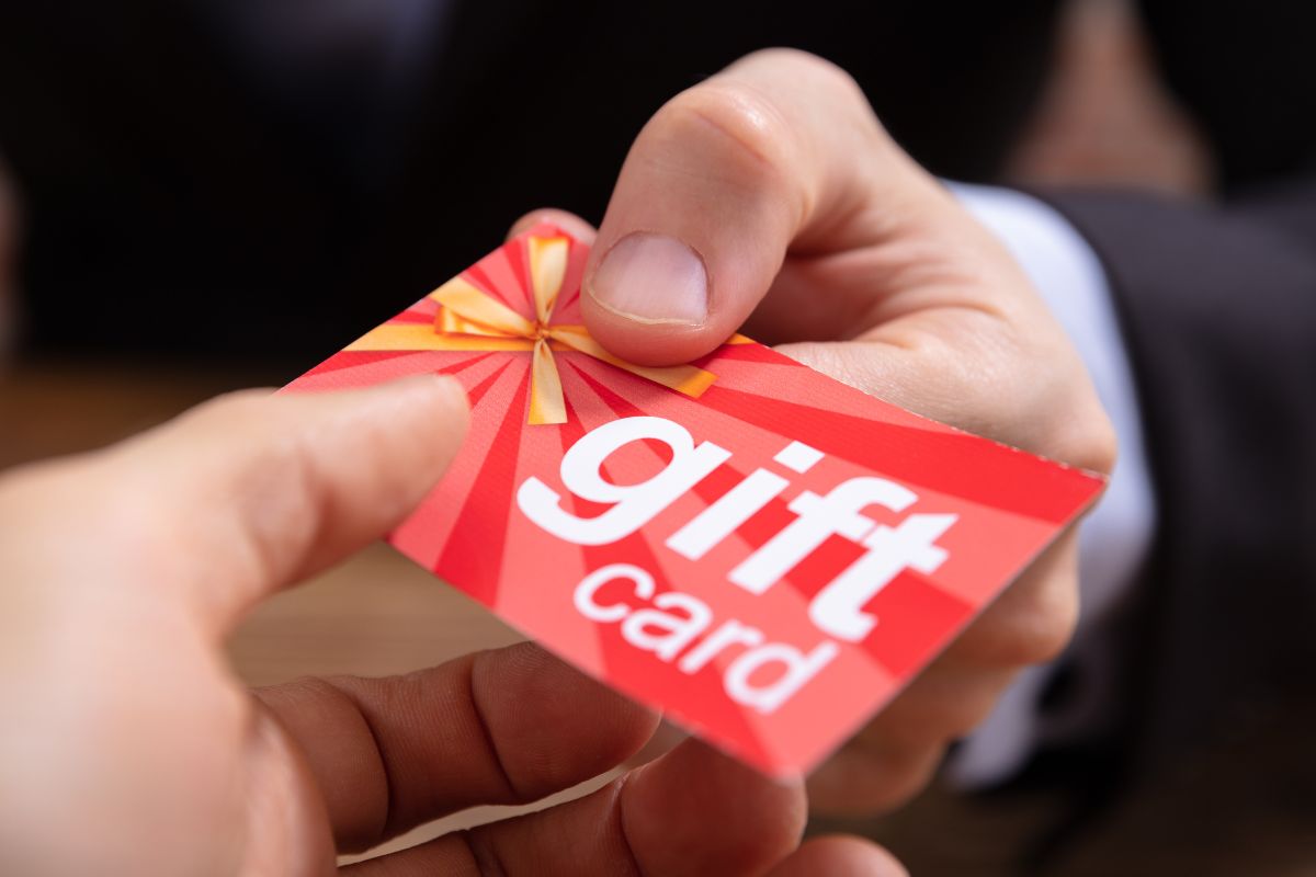 The image shows a man's hand handing over a gift card.